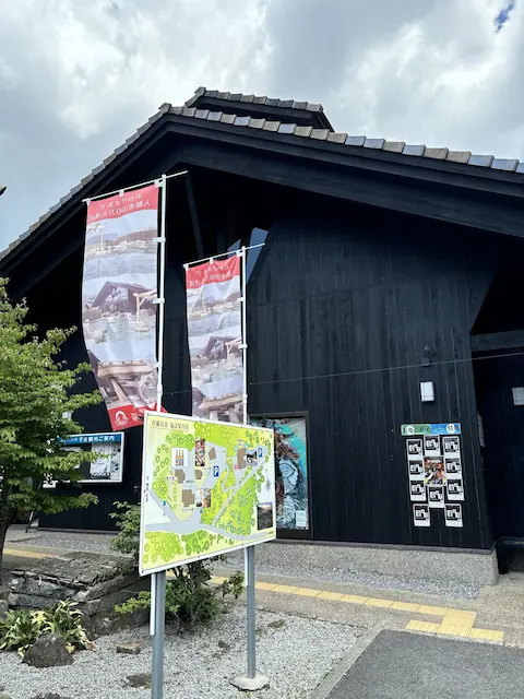 黒い建物の外観と周囲の緑、案内板がある風景