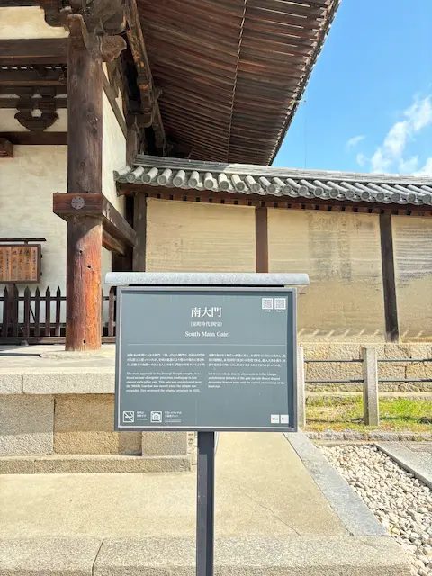 南大門の説明板がある風景、背後には屋根と壁が見える。