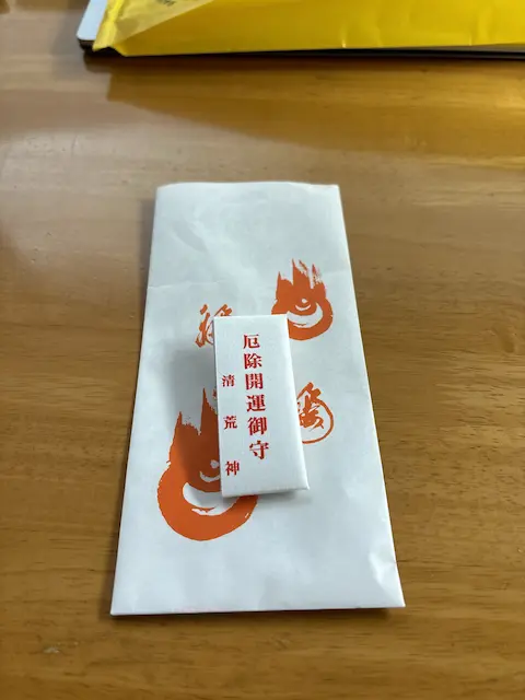 白い封筒の上に乗っかっている小さな御守りに、赤い文字で「厄除開運御守」と書かれています。